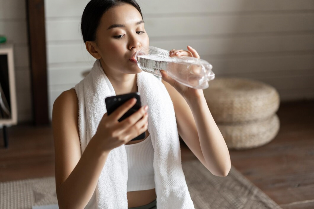 Девушка пьёт воду и мониторит приложение в смартфоне