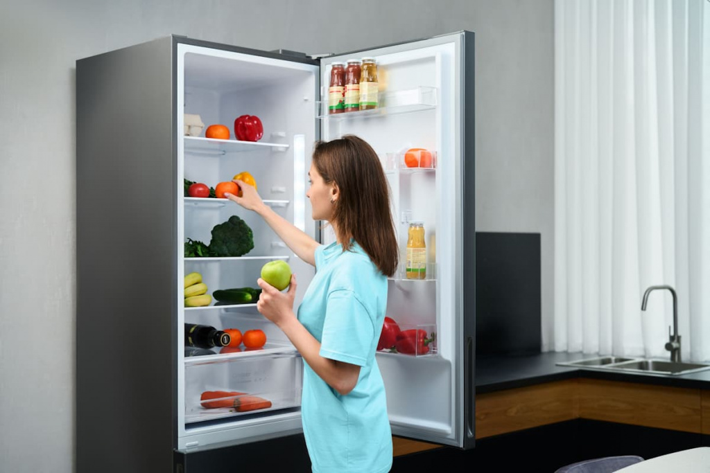 Девушка берет продукты из холодильника